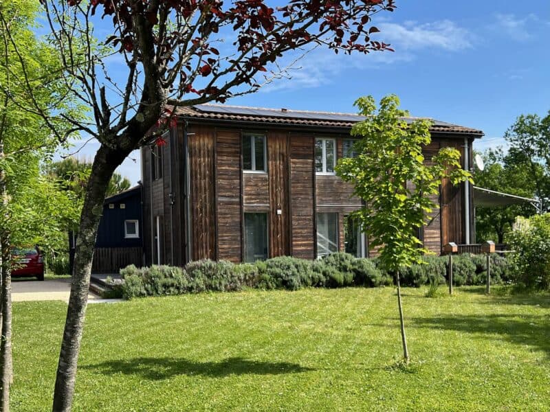 Façade en bois de la Maison Les Terrasses vue depuis le jardin arboré