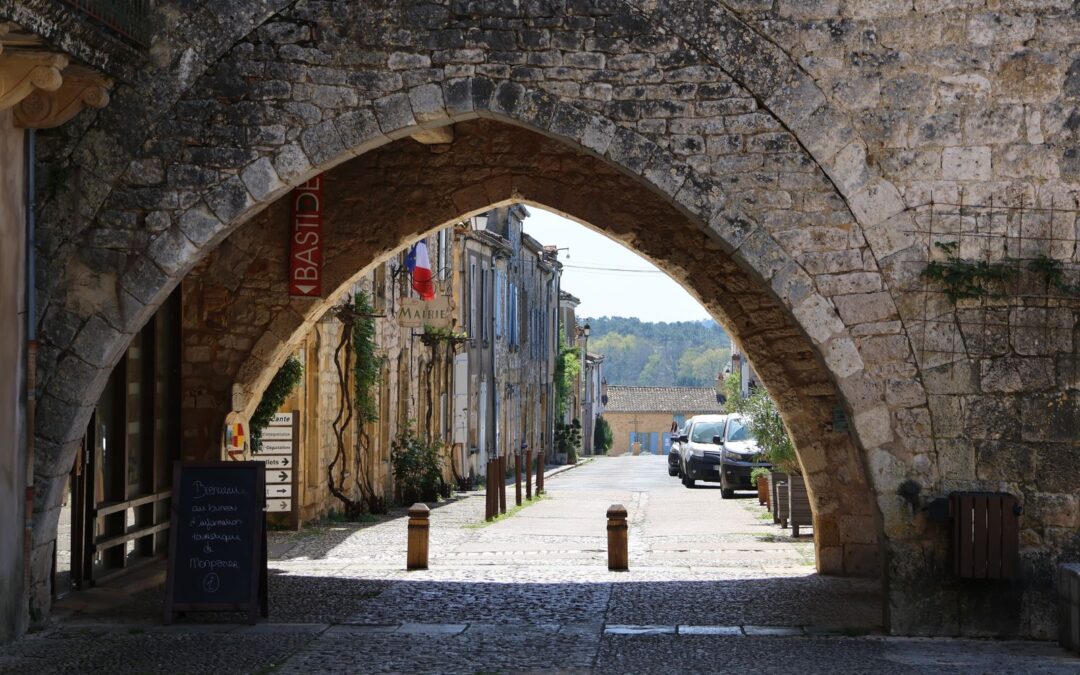 Porte fortifiée en pierre dorée et ruelle pavée d'une bastide du Sud-Ouest en fin d'été