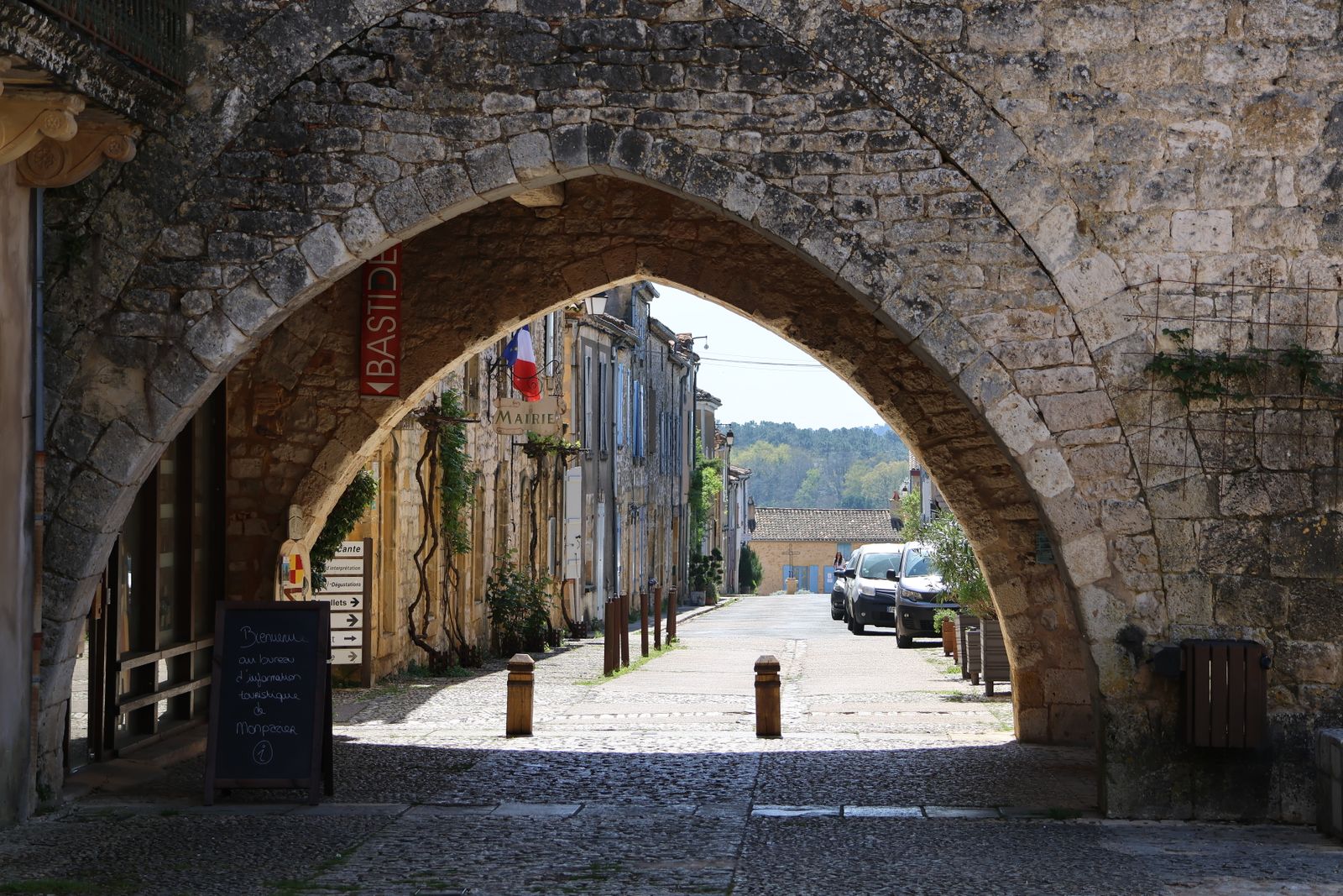 Porte fortifiée en pierre dorée et ruelle pavée d'une bastide du Sud-Ouest en fin d'été