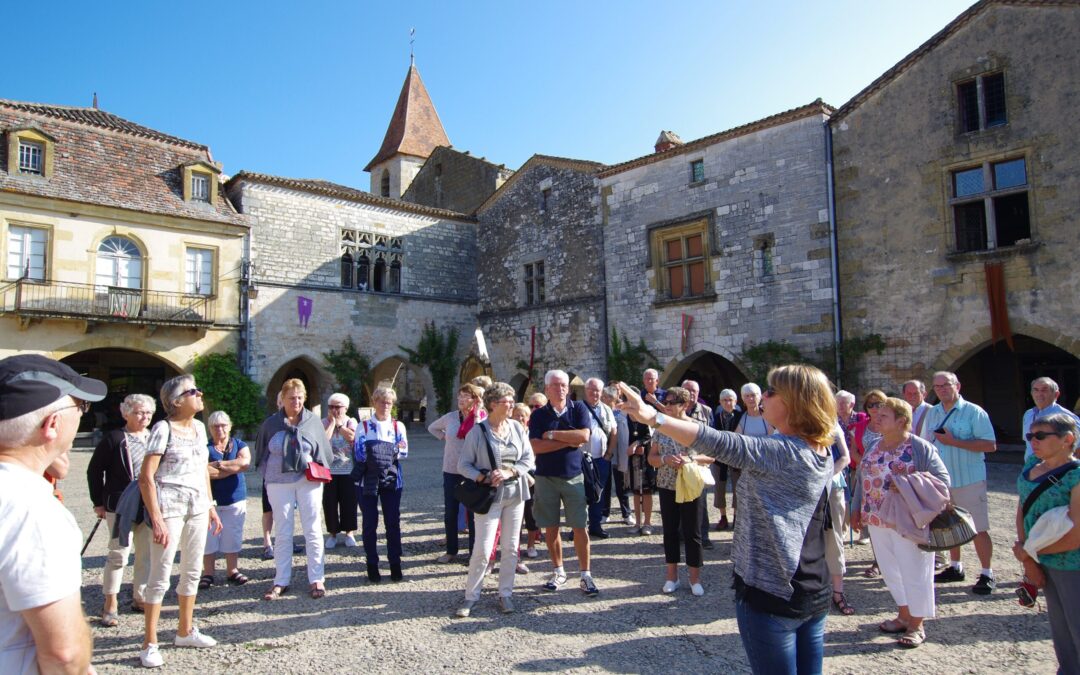 Guide conférencière commentant la place à arcades de la bastide de Monpazier devant un groupe de visiteurs