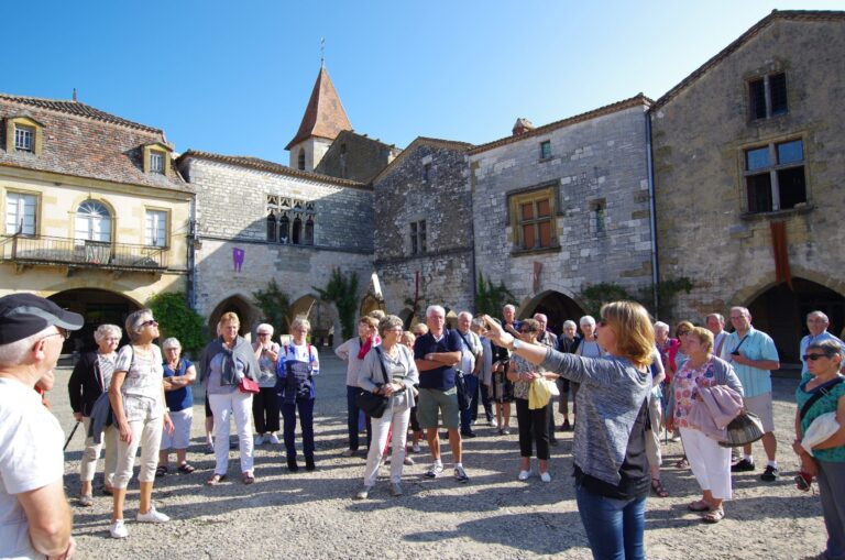 Guide conférencière commentant la place à arcades de la bastide de Monpazier devant un groupe de visiteurs